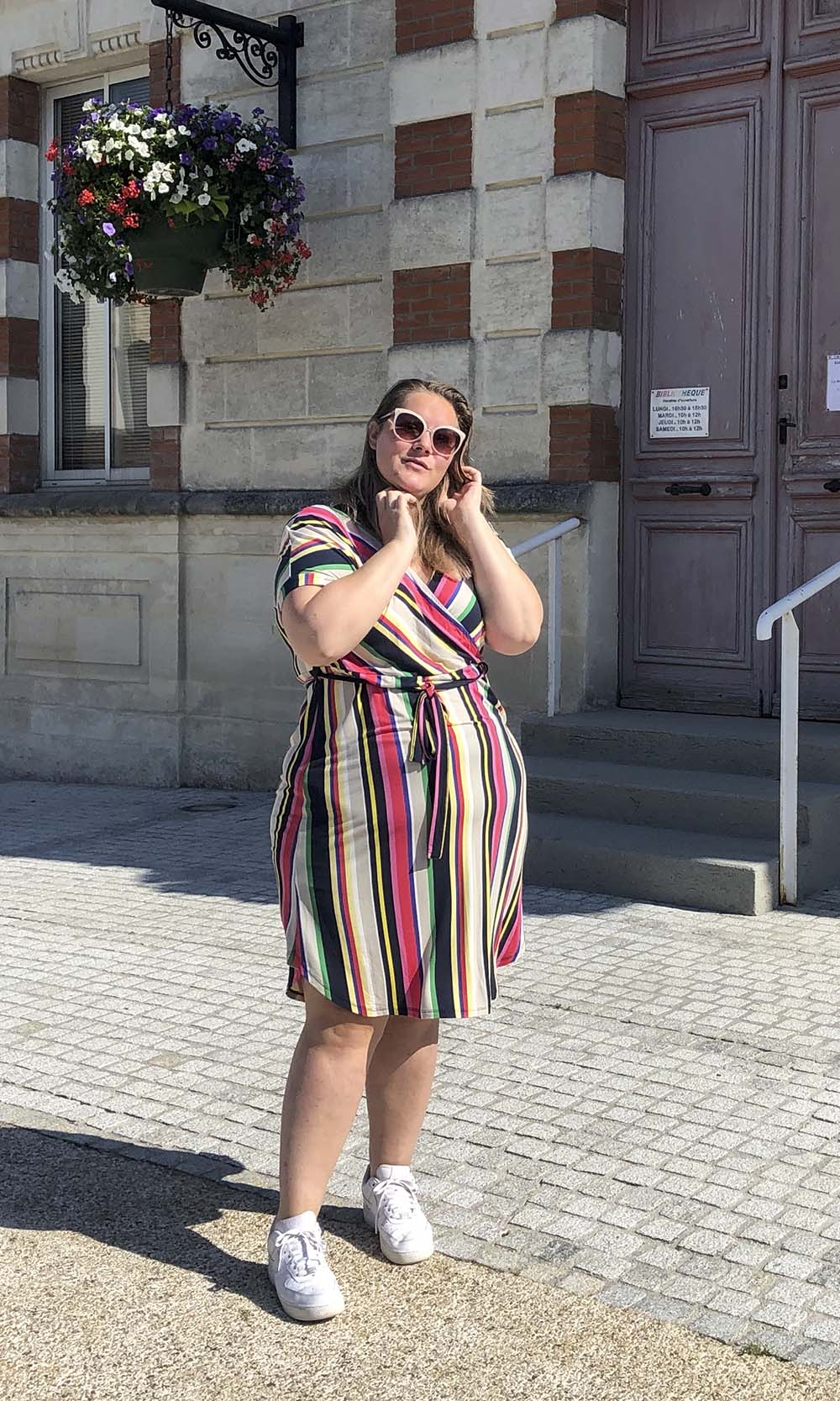 op een zonnige plein voor het gemeentehuis, in een gestreepte jurk met allerlei kleurtjes en een zonnebril op 